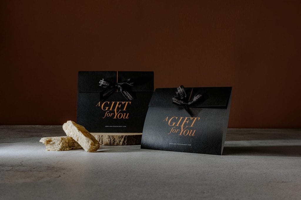 Two black Argyrides Winery gift card envelopes reading "A Gift for You," one larger and one smaller, with branded ribbon bows and pieces of nougat beside them