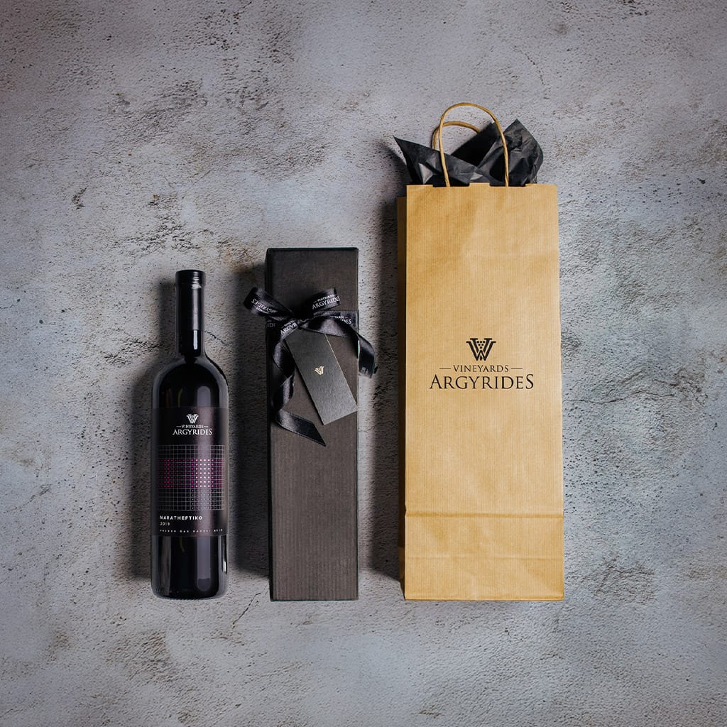 Argyrides Vineyards Maratheftiko bottle next to a black gift box with ribbon and tag, and a kraft paper wine bag with the winery logo